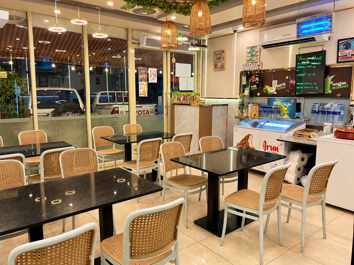 The Corner Meals dining area, with cane chairs, black tables and warm pendant lights.