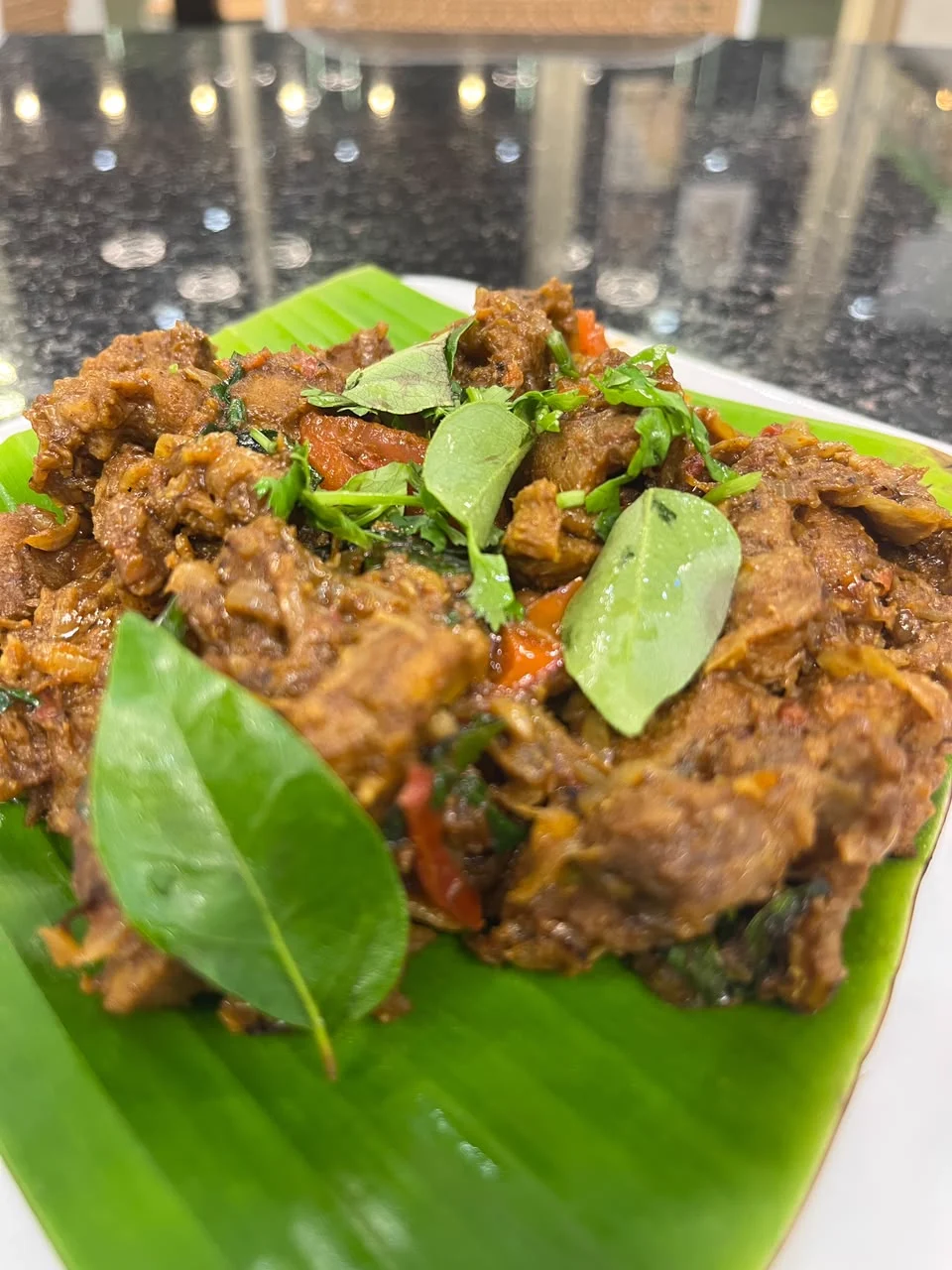 A roast dish garnished with curry leaves on a banana leaf.